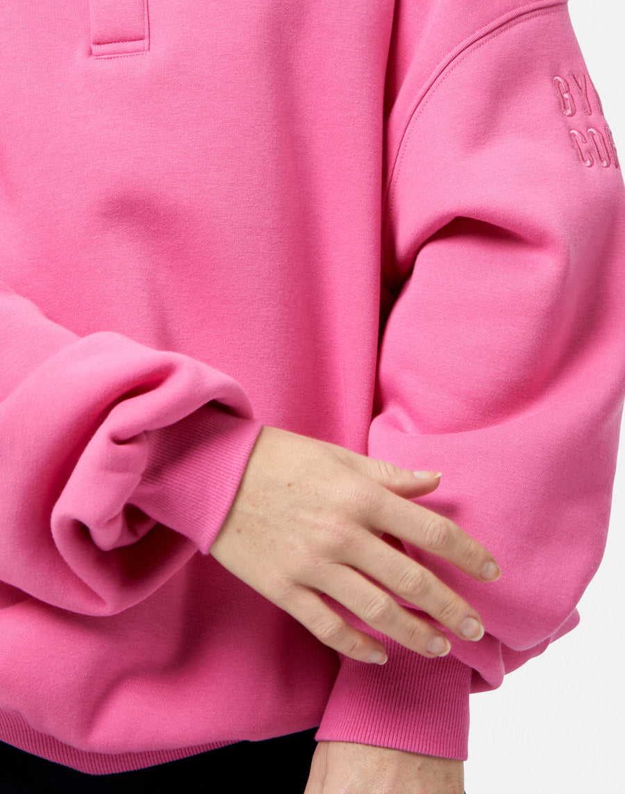 Close-up of a pink hoodie with a brand logo on the sleeve.